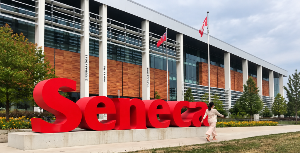 Woman walking beside the large red Seneca sign at Seneca Polytechnic in Toronto